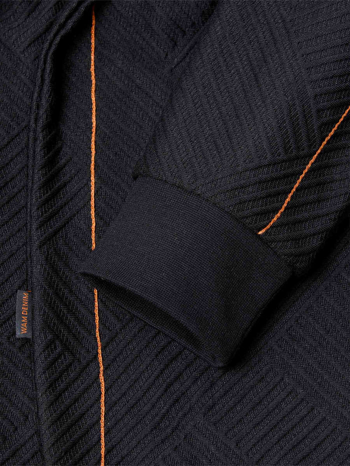 Close-up of sleeve and orange stitch detailing on black textured fabric – Wam Denim.