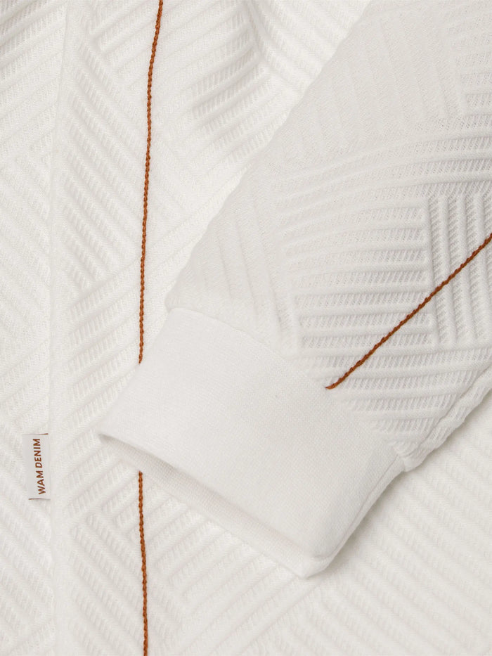 Close-up of white textured sweatshirt sleeve with brown stitching and cuff detail – Wam Denim.