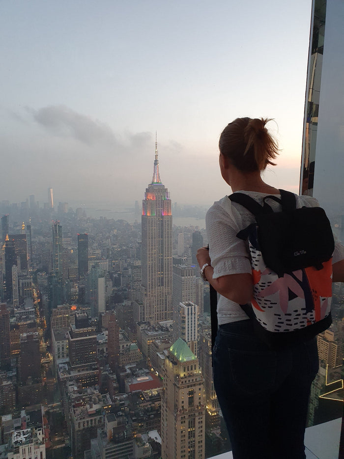 Ela Mo™ Daypack Rucksack | Papercut Tulip. Eine Frau mit dem Rucksack auf dem Rücken – alltäglicher Lifestyle.