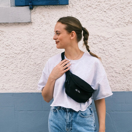 Ela Mo™ Hipbag  | Black. Eine Frau mit Hipbag an einem sonnigen Tag auf der Straße.