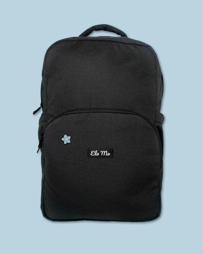Ela Mo™ Mini Pin für Rucksäcke | Vergissmeinnicht. Ein kleiner Pin ist vorne am schwarzen Rucksack befestigt.