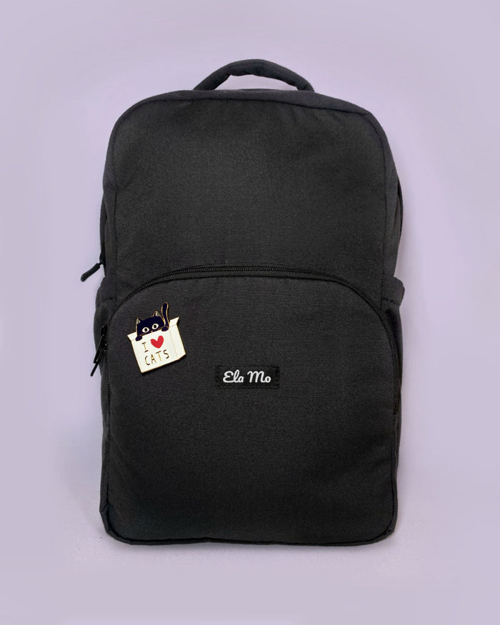 Ela Mo™ Pin für Rucksäcke | Cat. Ein kleiner Pin ist vorne am schwarzen Rucksack befestigt.