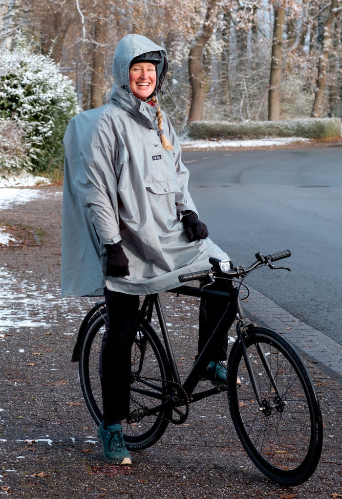 Ela Mo™ Regenponcho | Mint. Eine Frau mit Regenponcho und Fahrrad auf der Straße.