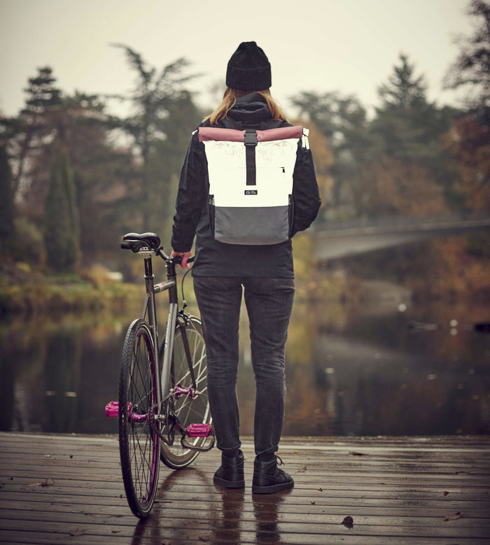 Ela Mo™ Rolltop Rucksack Night Edition | Peach.  Eine Frau mit dem reflektiven Rucksack auf dem Rücken im Freien.