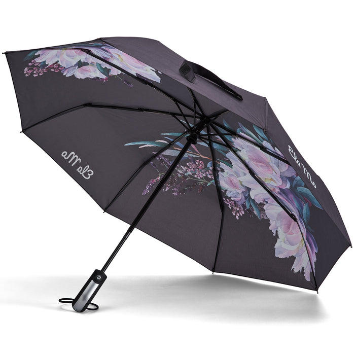 Ela Mo™ Taschenschirm | Beauty in Darkness. Ein schwarzer, geblümter Regenschirm mit Herstellerlogo darauf.