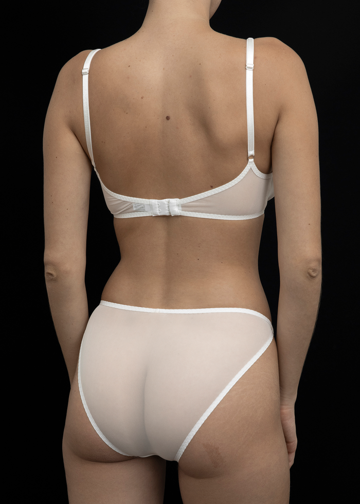 A view of the back of the Kye Intimates Mies Brief in the color bone. A sheer underwear with a high cut leg, and a flattering mid rise. Features an elegant overlap waist detail, and designed to hug your natural curves.