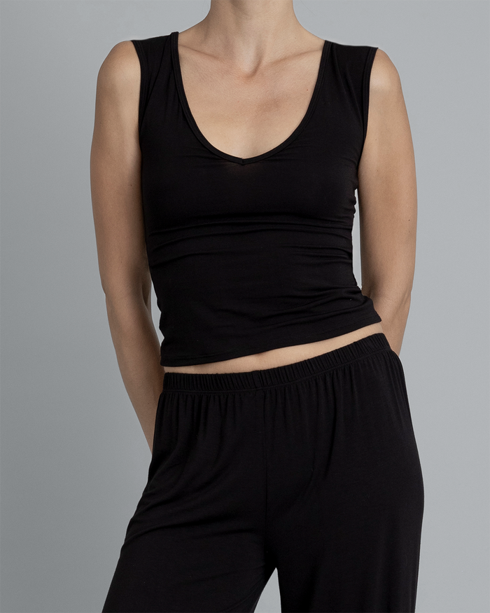 Close up of model wearing Kye Recline Shell bamboo v-neck fitted sleeveless tank in black paired with matching bamboo long pants. The ensemble offers a relaxed and stylish look, ideal for both lounging and casual outings by Kye Intimates.
