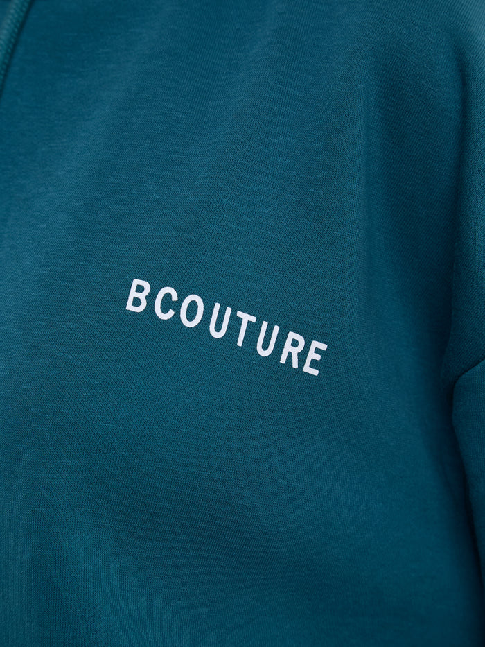 Close-up of a teal blue sweatshirt featuring the word 'BCOUTURE' printed in white across the chest.