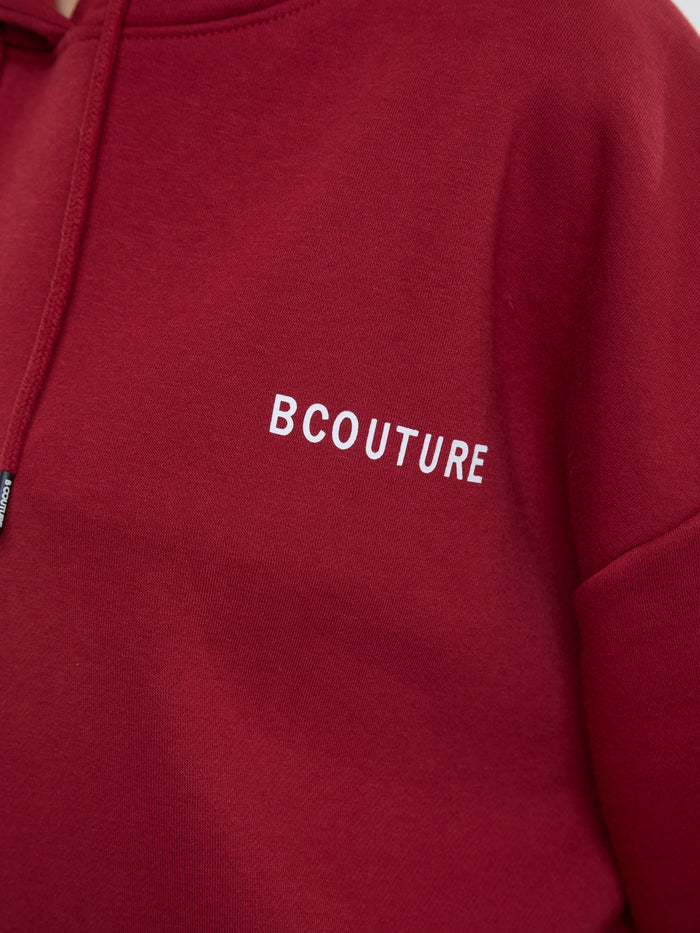 A close-up of a red hoodie featuring the brand name 'BCOUTURE' embroidered in white capital letters on the chest.